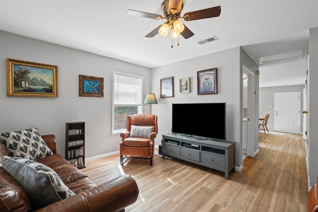 living area featuring light wood finished floors, visible vents, baseboards, attic access, and ceiling fan