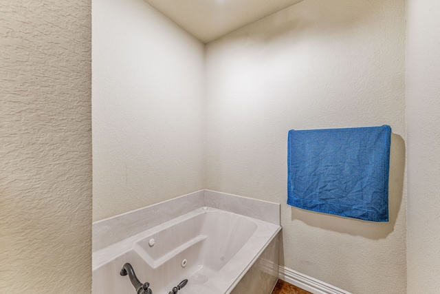 full bathroom with a textured wall, baseboards, and a jetted tub
