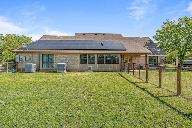 back of property featuring a fenced backyard, solar panels, central air condition unit, brick siding, and a yard