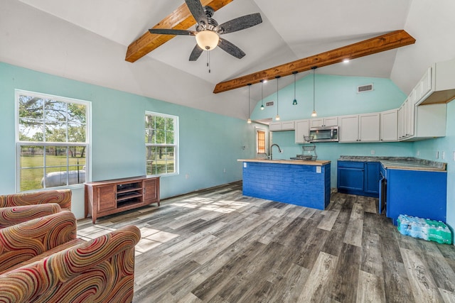 kitchen featuring wood finished floors, white cabinets, ceiling fan, beamed ceiling, and stainless steel microwave