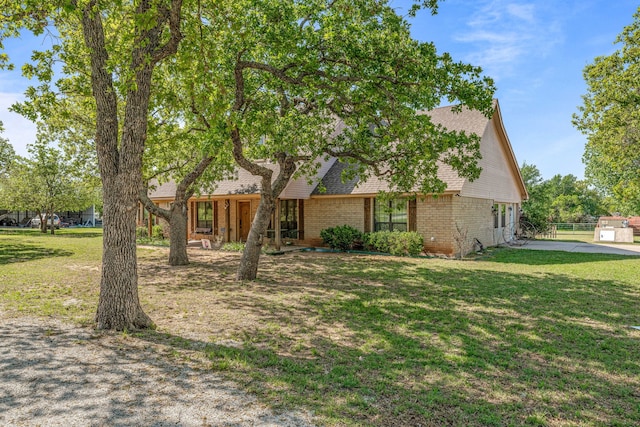 view of property hidden behind natural elements with a front lawn, brick siding, and roof with shingles