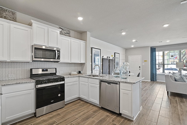 kitchen featuring a peninsula, a sink, white cabinetry, wood finish floors, and appliances with stainless steel finishes
