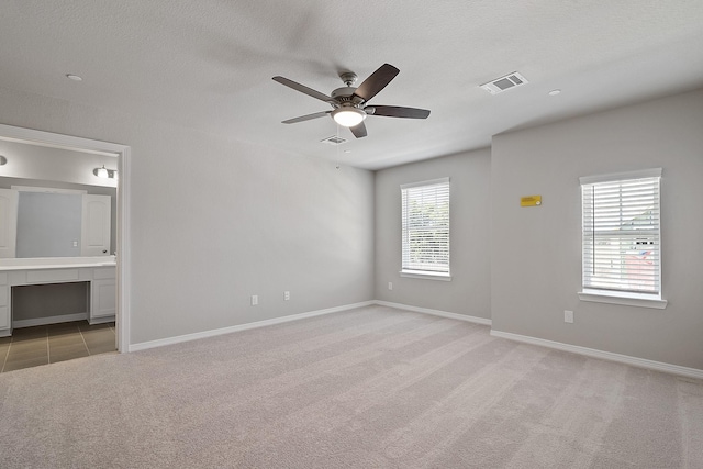 spare room with light colored carpet, baseboards, a ceiling fan, and visible vents