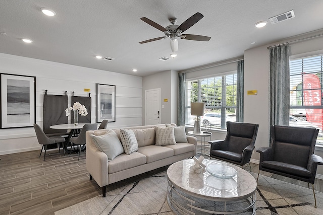 living area with baseboards, wood finished floors, visible vents, and a ceiling fan