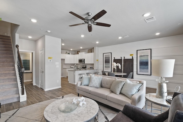 living room with stairway, wood tiled floor, ceiling fan, baseboards, and visible vents