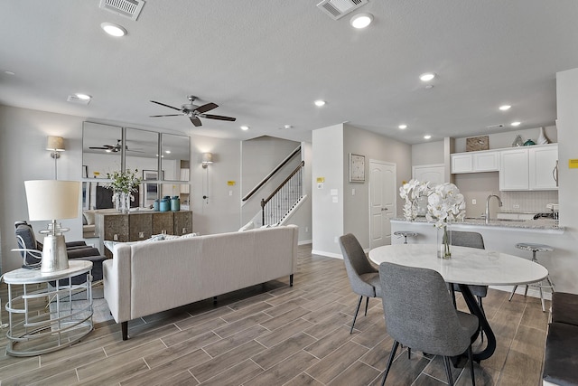 living room with stairway, visible vents, baseboards, and ceiling fan