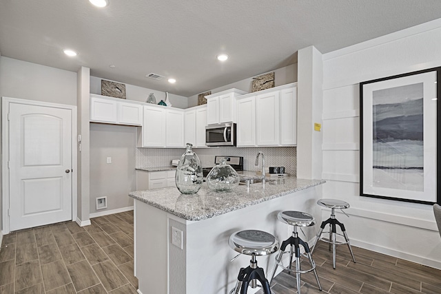 kitchen featuring stainless steel microwave, visible vents, white cabinetry, light stone countertops, and wood finish floors