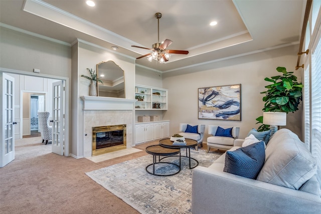carpeted living room featuring crown molding, a raised ceiling, a tiled fireplace, ceiling fan, and recessed lighting
