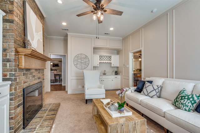 living area with a decorative wall, ceiling fan, a brick fireplace, light carpet, and crown molding