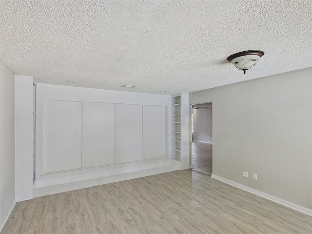 spare room featuring wood finished floors, a textured ceiling, built in shelves, and baseboards