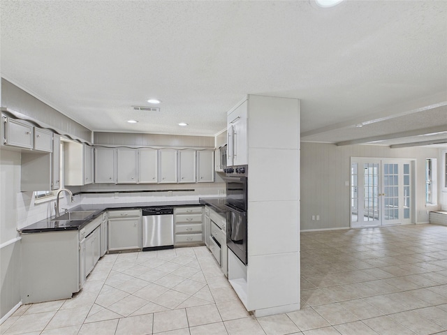 kitchen with stainless steel dishwasher, dark countertops, a sink, light tile patterned floors, and visible vents