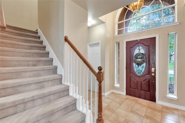 entryway featuring a towering ceiling, light tile patterned floors, baseboards, an inviting chandelier, and stairs