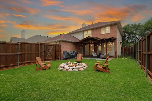 back of property at dusk with a lawn, brick siding, a fenced backyard, an outdoor living space with a fire pit, and a patio