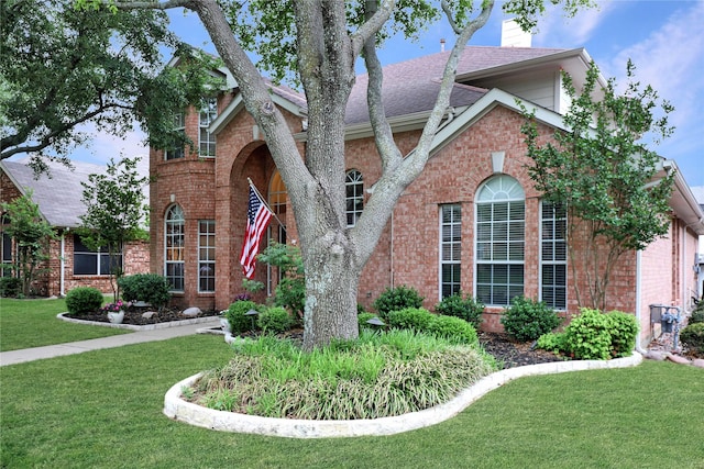 traditional-style house featuring brick siding, a front yard, and roof with shingles
