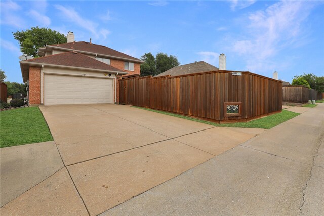 view of side of property featuring brick siding, an attached garage, fence, and driveway
