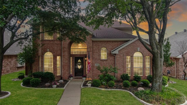 traditional-style house featuring a shingled roof, a front lawn, and brick siding