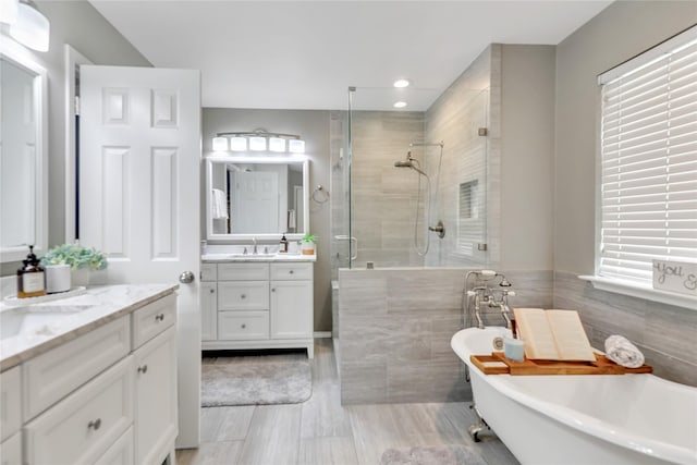 bathroom with a sink, recessed lighting, a freestanding tub, a shower stall, and two vanities