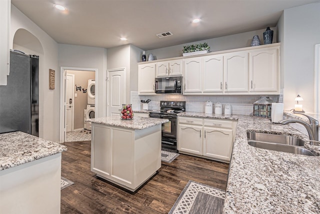 kitchen with white cabinets, stacked washer and dryer, a sink, visible vents, and black appliances