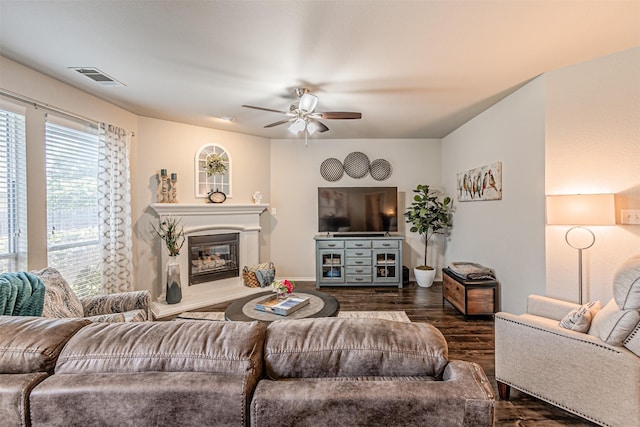 living area with visible vents, dark wood-style flooring, baseboards, a glass covered fireplace, and ceiling fan