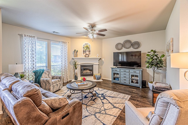 living area featuring a ceiling fan, a glass covered fireplace, dark wood finished floors, baseboards, and visible vents