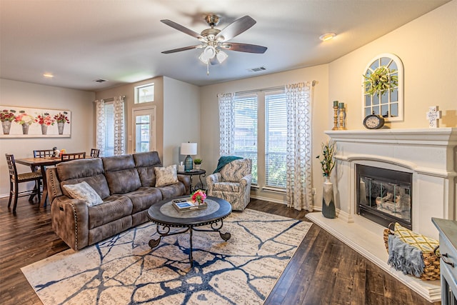 living area with wood finished floors, visible vents, baseboards, a glass covered fireplace, and ceiling fan