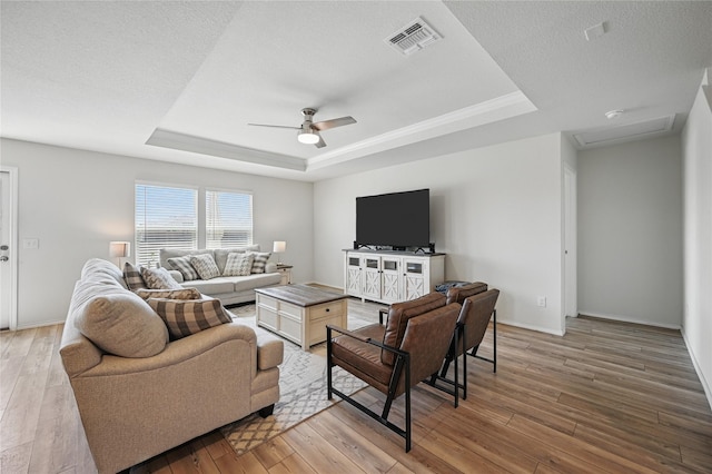 living area with a raised ceiling, visible vents, light wood-style floors, baseboards, and ceiling fan