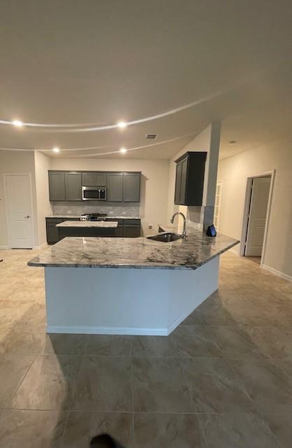 702 Grassland Way, Arlington, TX 76002 - kitchen with stainless steel microwave, gray cabinets, light stone countertops, stove, and a peninsula