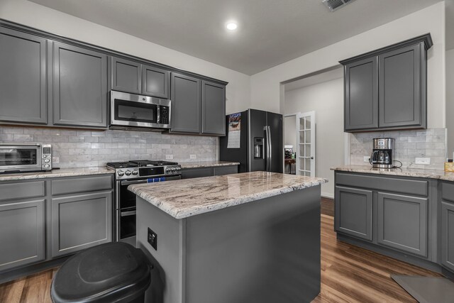 702 Grassland Way, Arlington, TX 76002 - kitchen featuring gray cabinets, appliances with stainless steel finishes, wood finished floors, a kitchen bar, and light stone countertops