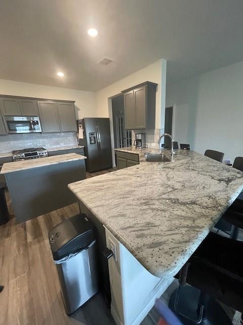 702 Grassland Way, Arlington, TX 76002 - kitchen featuring stainless steel appliances, gray cabinets, a breakfast bar area, a peninsula, and wood finished floors