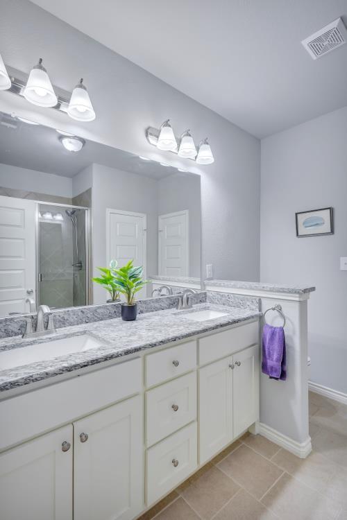 full bath featuring tile patterned floors, a sink, double vanity, visible vents, and a shower stall