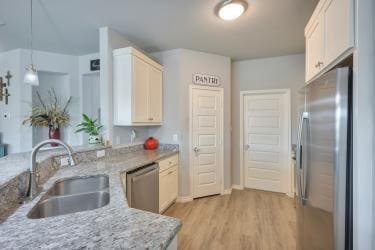 kitchen featuring stainless steel appliances, a sink, light wood-type flooring, pendant lighting, and light stone counters