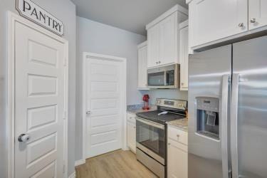 kitchen with light countertops, light wood finished floors, appliances with stainless steel finishes, and white cabinetry
