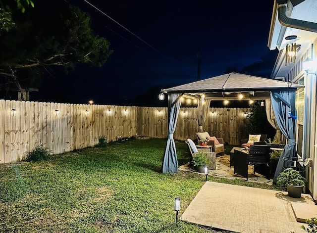 yard at night featuring an outdoor living space, a fenced backyard, a gazebo, and a patio
