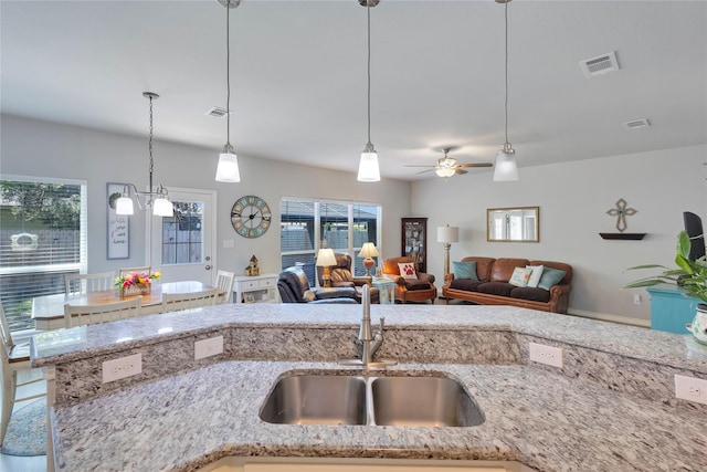 kitchen featuring a sink, visible vents, light stone counters, ceiling fan, and decorative light fixtures