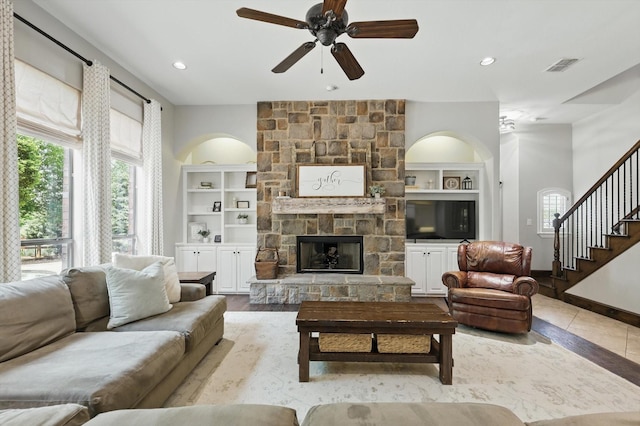 living room with stairway, a ceiling fan, built in shelves, a fireplace, and visible vents