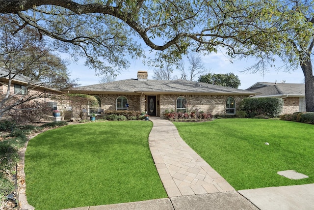 ranch-style house with brick siding, roof with shingles, a chimney, and a front yard