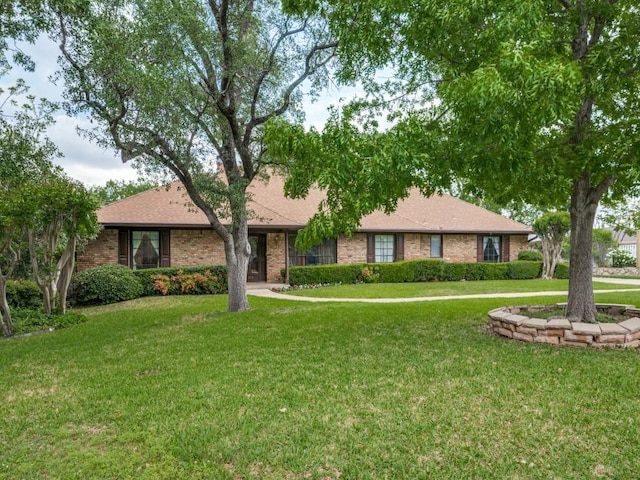 ranch-style house with a shingled roof, a front lawn, and brick siding