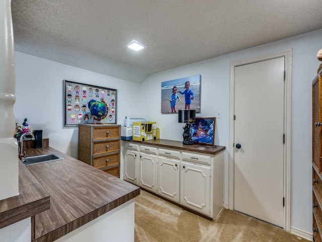 interior space featuring a sink, butcher block countertops, light carpet, lofted ceiling, and white cabinetry