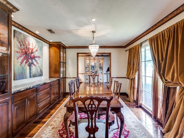 dining area with dark wood finished floors, visible vents, crown molding, baseboards, and a notable chandelier