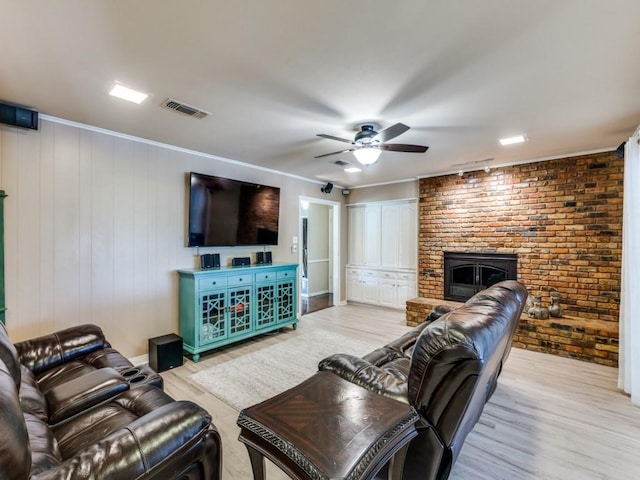 living area with light wood finished floors, visible vents, brick wall, a ceiling fan, and a brick fireplace