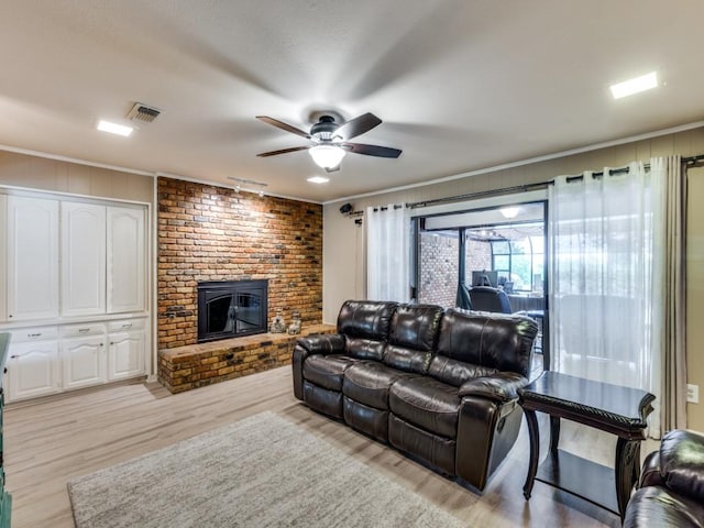 living room with light wood-style flooring, ceiling fan, a fireplace, ornamental molding, and visible vents
