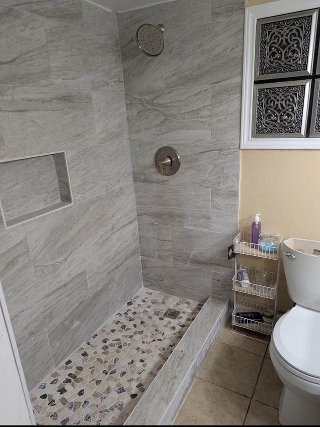 full bathroom with toilet, tile patterned floors, and a tile shower