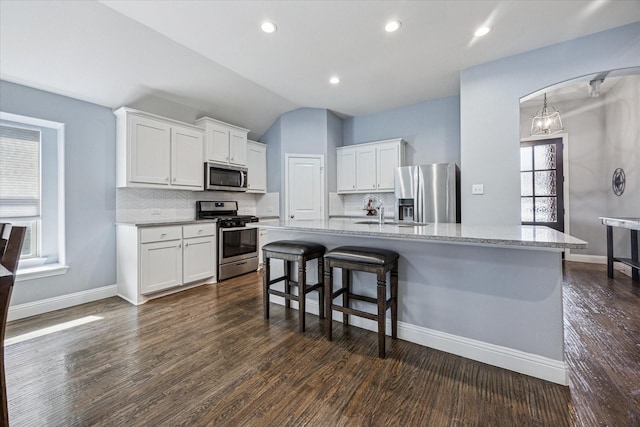 kitchen featuring white cabinets, a kitchen breakfast bar, backsplash, baseboards, and appliances with stainless steel finishes