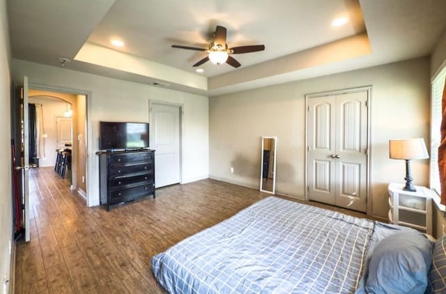 bedroom featuring dark wood finished floors, a raised ceiling, arched walkways, baseboards, and ceiling fan