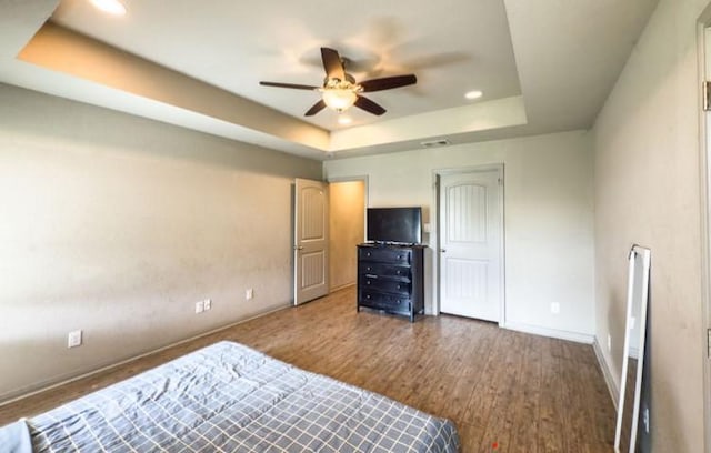 bedroom featuring wood finished floors, ceiling fan, a raised ceiling, baseboards, and recessed lighting