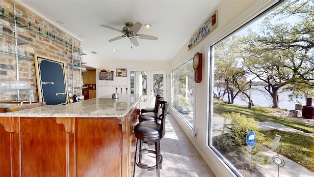 1351 Porter Ct, Granbury, TX 76048 - kitchen with light stone counters, a ceiling fan, french doors, light tile patterned floors, and a breakfast bar area