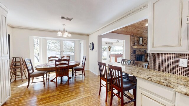 1351 Porter Ct, Granbury, TX 76048 - dining room with crown molding, a chandelier, light wood finished floors, a fireplace, and visible vents
