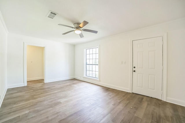 empty room with wood finished floors, visible vents, a ceiling fan, and ornamental molding