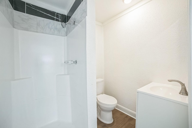 bathroom featuring wood finished floors, toilet, vanity, baseboards, and a shower