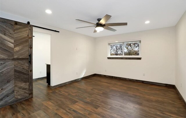 spare room featuring a barn door, recessed lighting, a ceiling fan, baseboards, and dark wood-style flooring